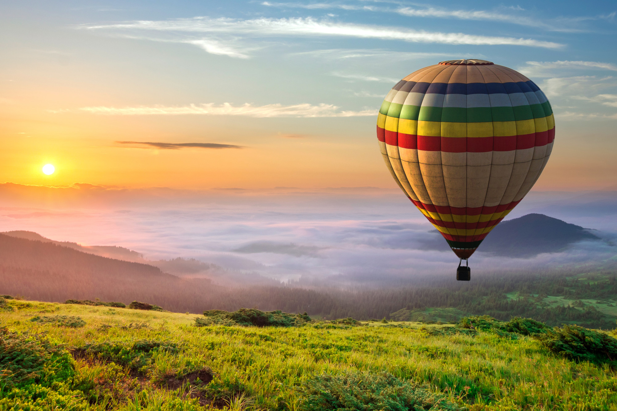 Big hot air baloon over idyllic landscape with green grass cover
